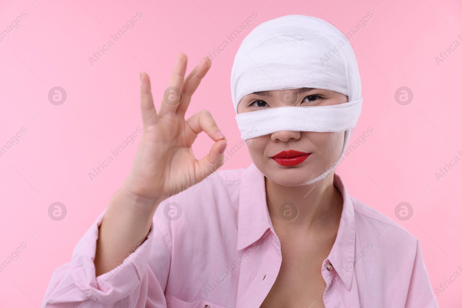 Photo of Woman with nose wrapped in medical bandage after plastic surgery operation on pink background