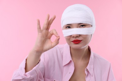 Woman with nose wrapped in medical bandage after plastic surgery operation on pink background