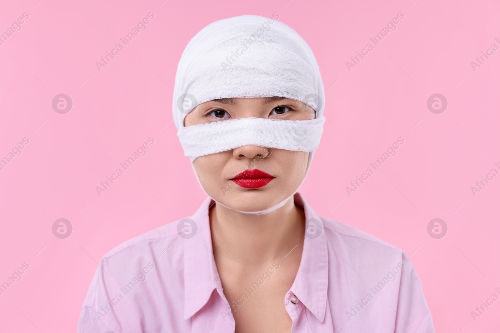 Photo of Woman with nose wrapped in medical bandage after plastic surgery operation on pink background