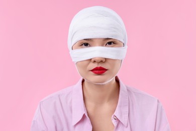 Woman with nose wrapped in medical bandage after plastic surgery operation on pink background