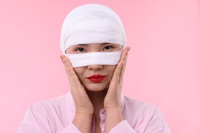 Woman with nose wrapped in medical bandage after plastic surgery operation on pink background