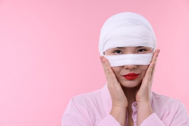 Woman with nose wrapped in medical bandage after plastic surgery operation on pink background. Space for text