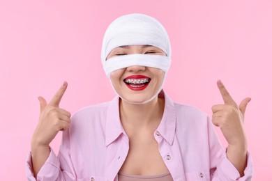 Photo of Woman with nose wrapped in medical bandage after plastic surgery operation on pink background