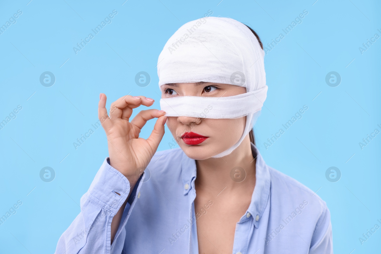 Photo of Woman with nose wrapped in medical bandage after plastic surgery operation on light blue background