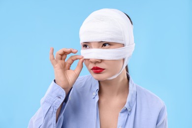 Woman with nose wrapped in medical bandage after plastic surgery operation on light blue background