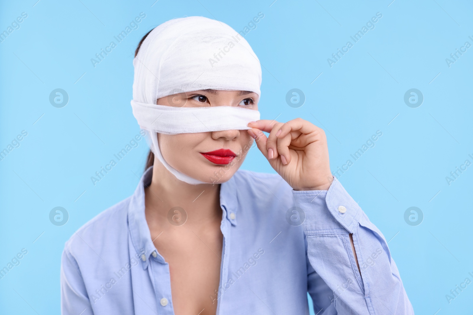 Photo of Woman with nose wrapped in medical bandage after plastic surgery operation on light blue background