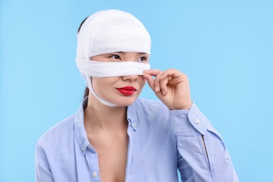 Woman with nose wrapped in medical bandage after plastic surgery operation on light blue background