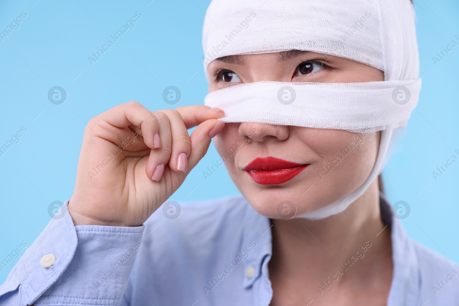 Photo of Woman with nose wrapped in medical bandage after plastic surgery operation on light blue background, closeup