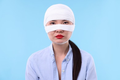 Photo of Woman with nose wrapped in medical bandage after plastic surgery operation on light blue background