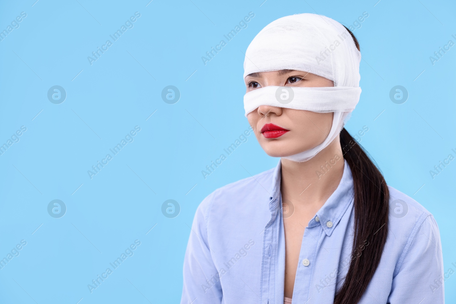 Photo of Woman with nose wrapped in medical bandage after plastic surgery operation on light blue background. Space for text