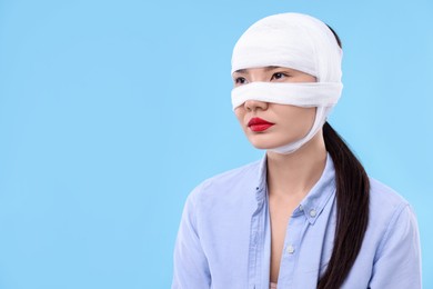 Woman with nose wrapped in medical bandage after plastic surgery operation on light blue background. Space for text