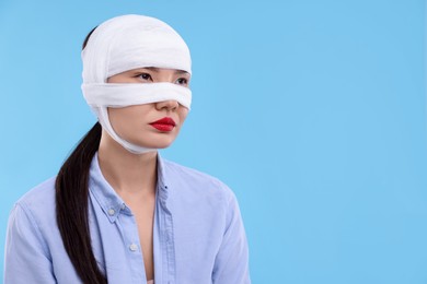 Photo of Woman with nose wrapped in medical bandage after plastic surgery operation on light blue background. Space for text