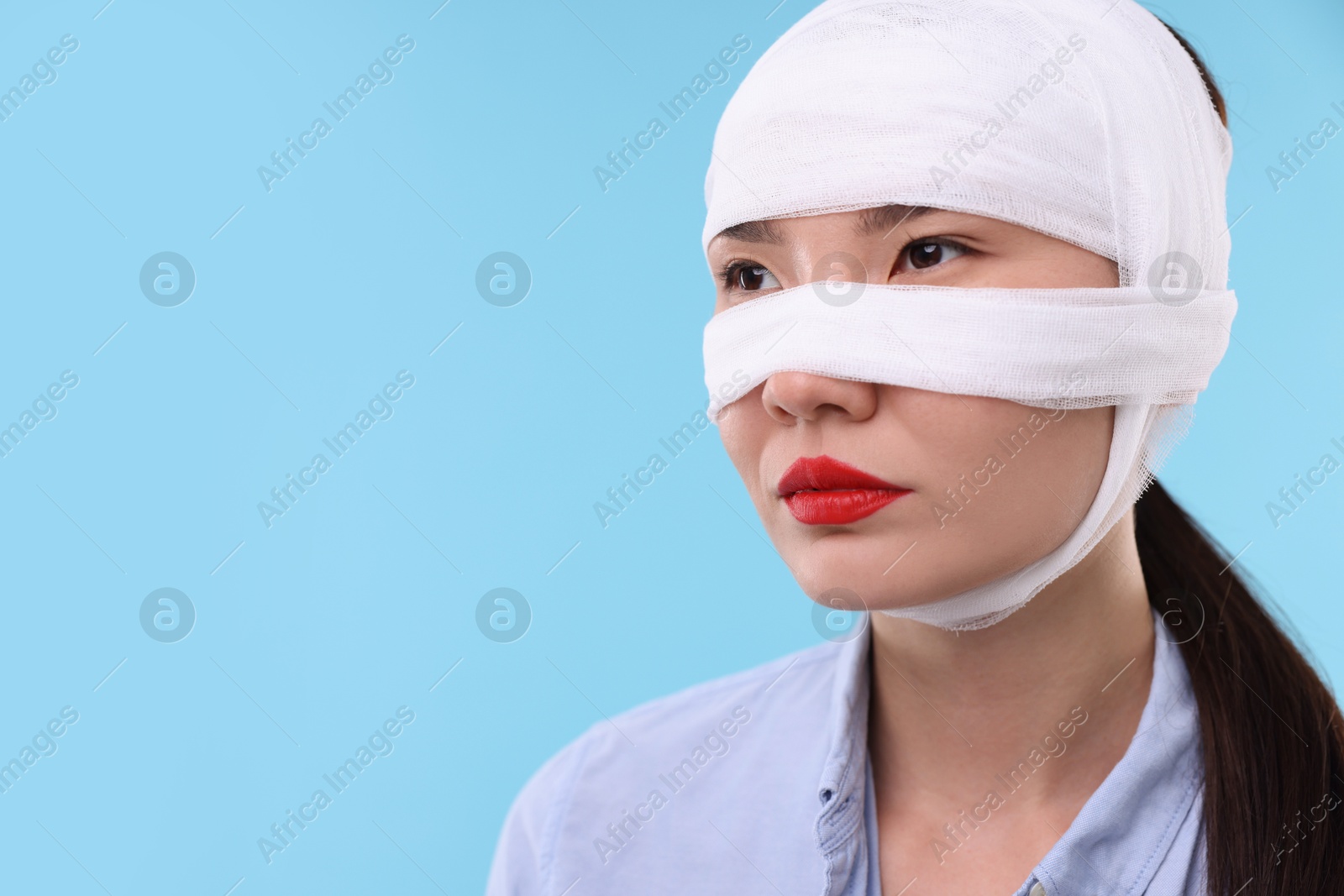 Photo of Woman with nose wrapped in medical bandage after plastic surgery operation on light blue background. Space for text