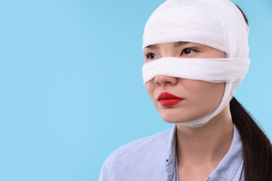 Photo of Woman with nose wrapped in medical bandage after plastic surgery operation on light blue background. Space for text