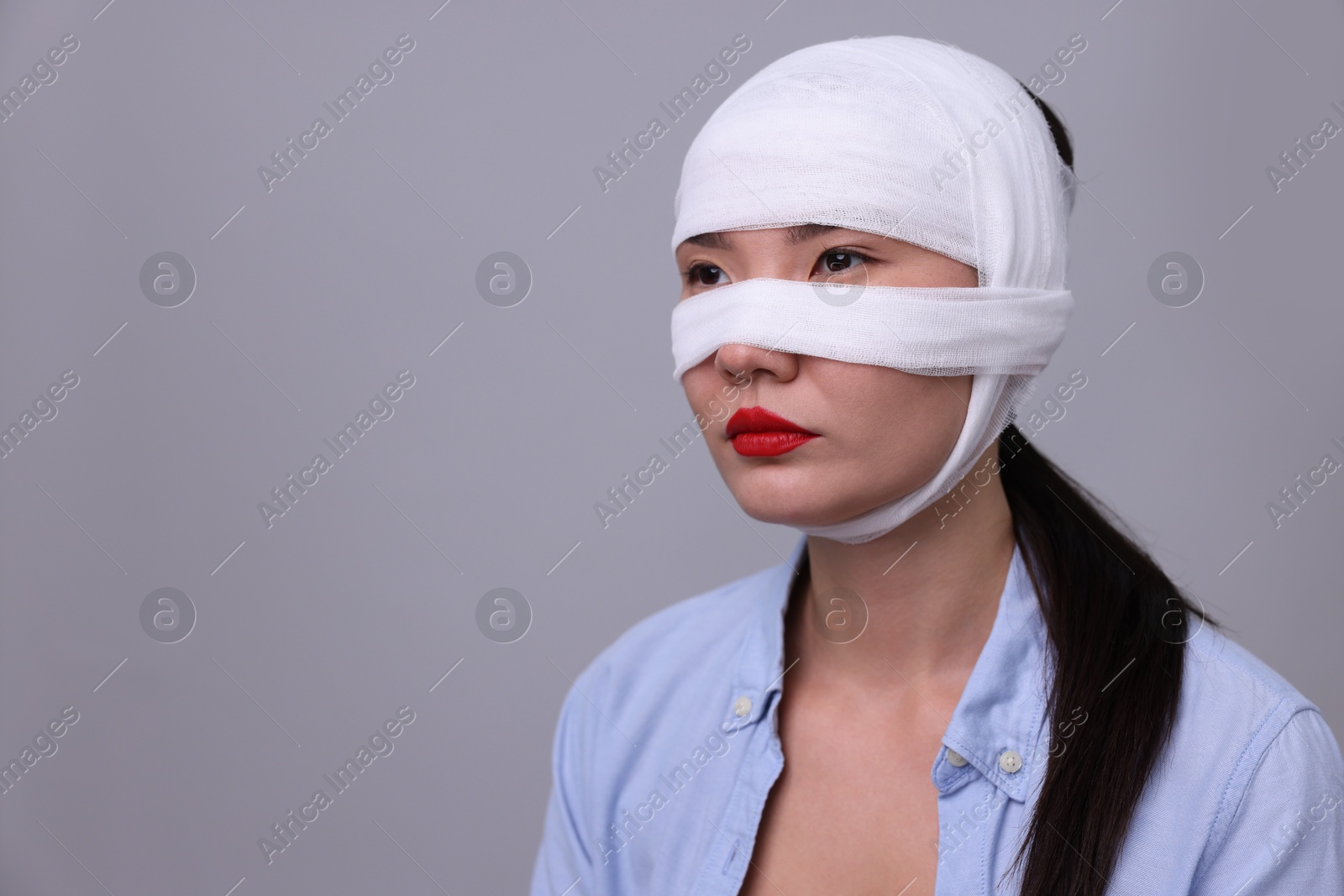 Photo of Woman with nose wrapped in medical bandage after plastic surgery operation on light grey background. Space for text