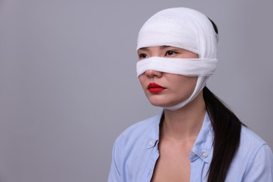 Woman with nose wrapped in medical bandage after plastic surgery operation on light grey background. Space for text