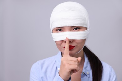 Photo of Woman with nose wrapped in medical bandage after plastic surgery operation making silent gesture on light grey background