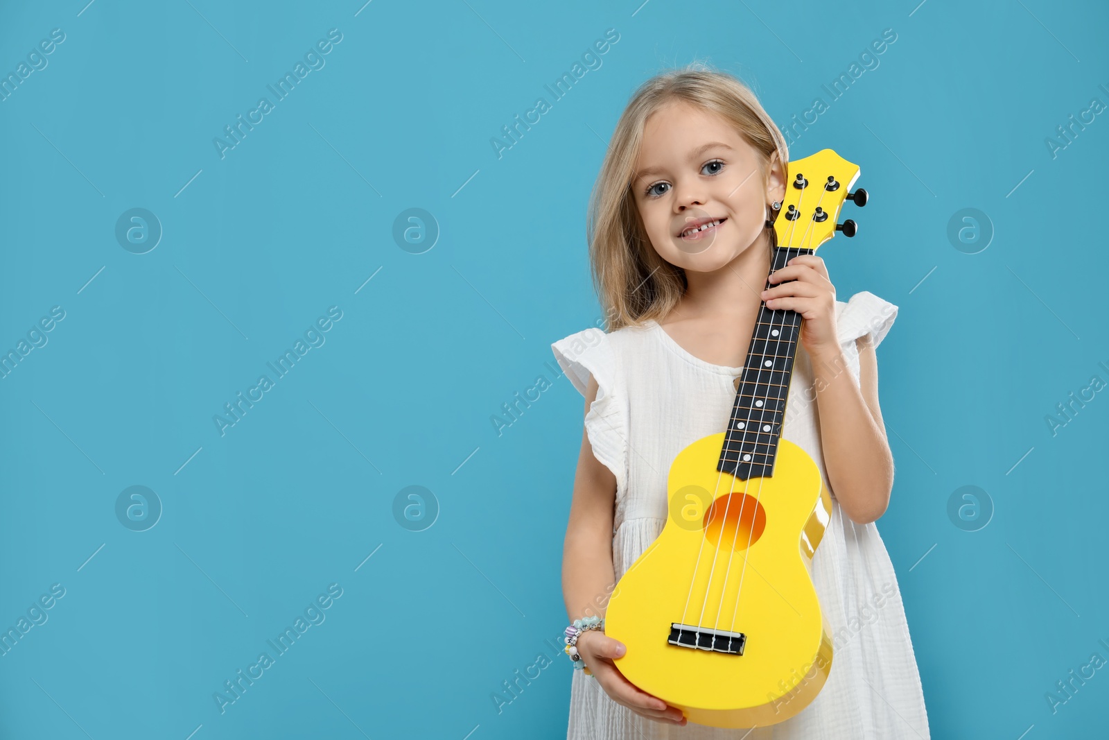 Photo of Little girl with ukulele on light blue background, space for text