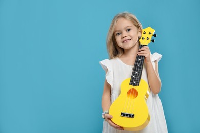 Photo of Little girl with ukulele on light blue background, space for text