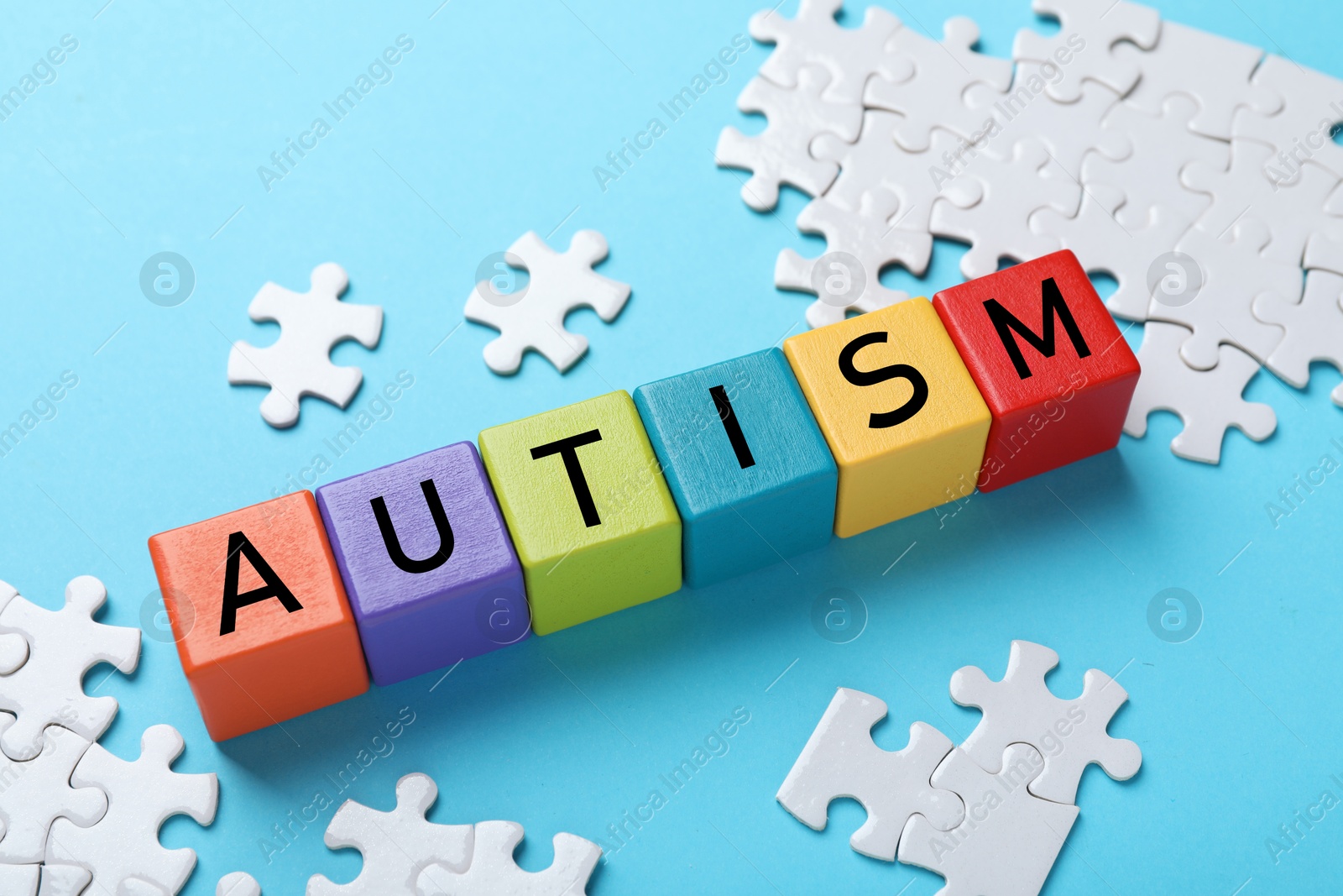 Photo of Word Autism made of colorful cubes and puzzle on light blue background