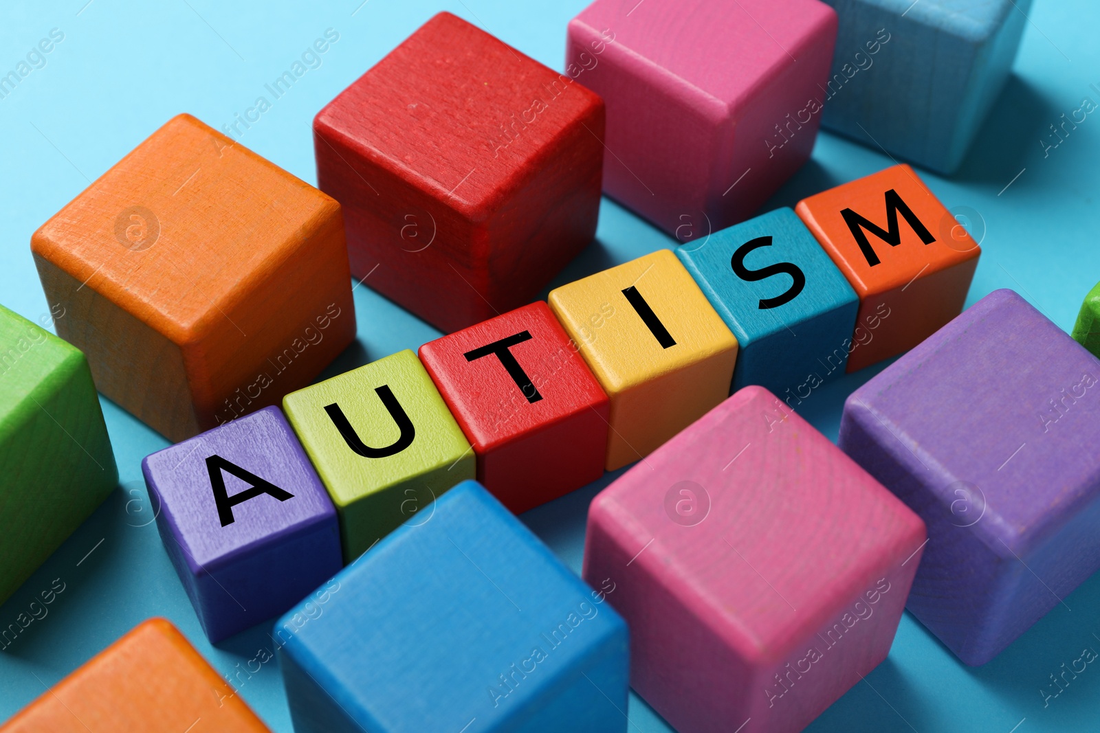 Photo of Word Autism made of colorful cubes on light blue background, closeup