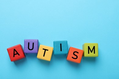 Photo of Word Autism made of colorful cubes on light blue background, top view