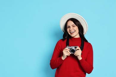 Photo of Young tourist in hat with camera on light blue background, space for text