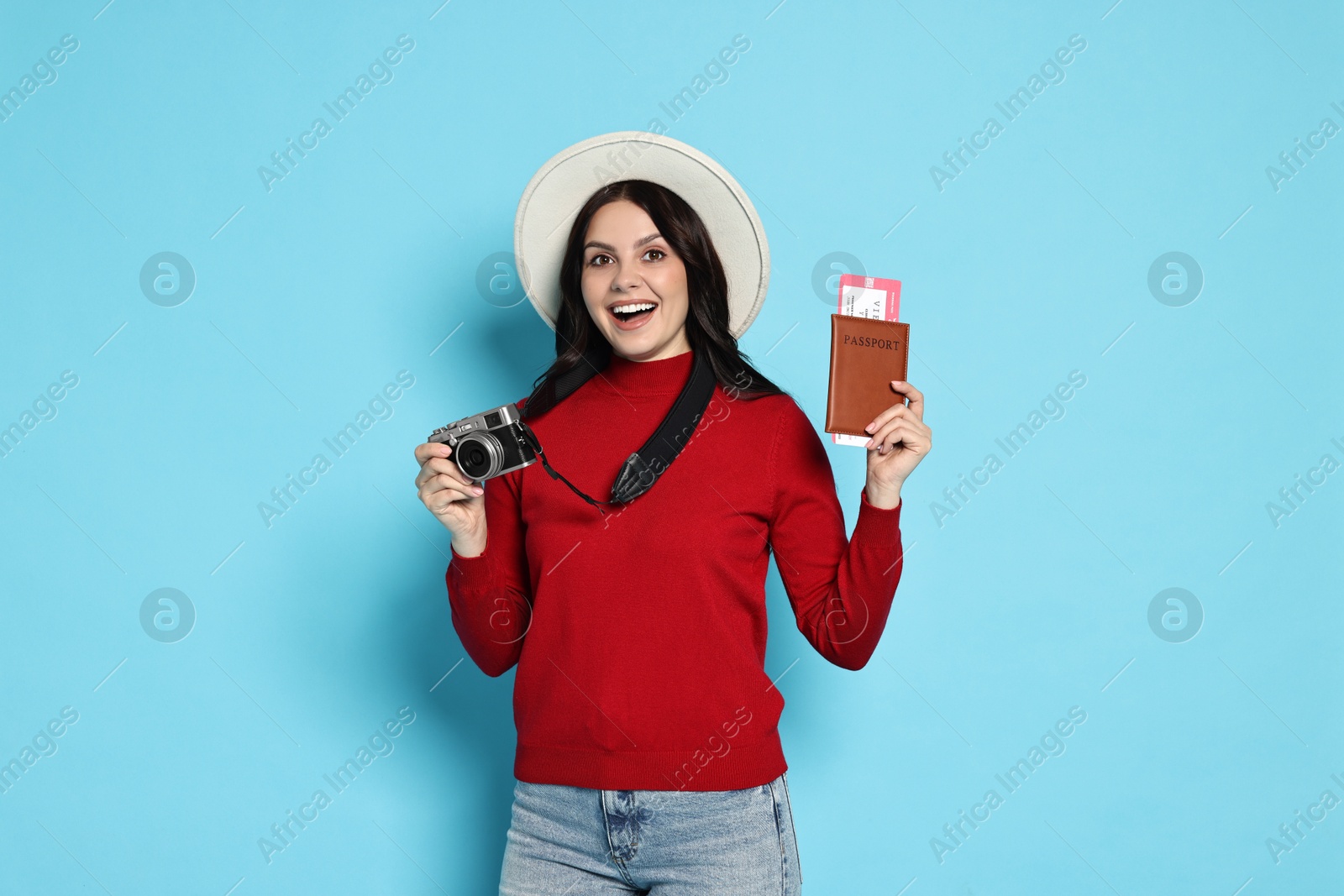 Photo of Young tourist in hat with camera, passport and tickets on light blue background