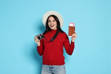 Young tourist in hat with camera, passport and tickets on light blue background