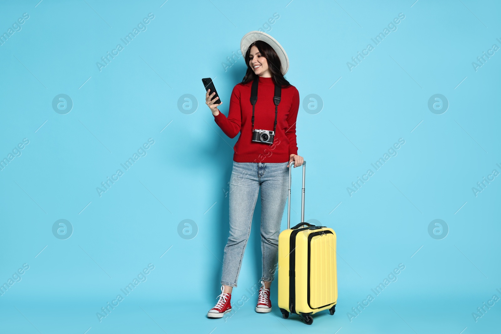 Photo of Young tourist in hat with camera, phone and suitcase on light blue background