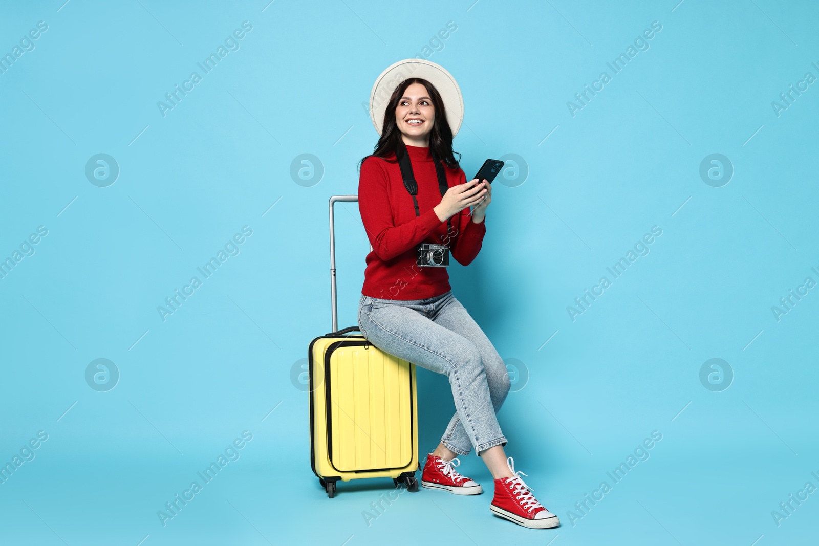 Photo of Young tourist in hat with camera, phone and suitcase on light blue background