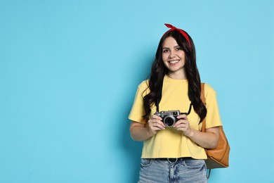 Young tourist with camera and backpack on light blue background, space for text