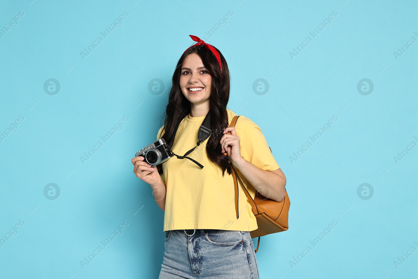 Photo of Young tourist with camera and backpack on light blue background