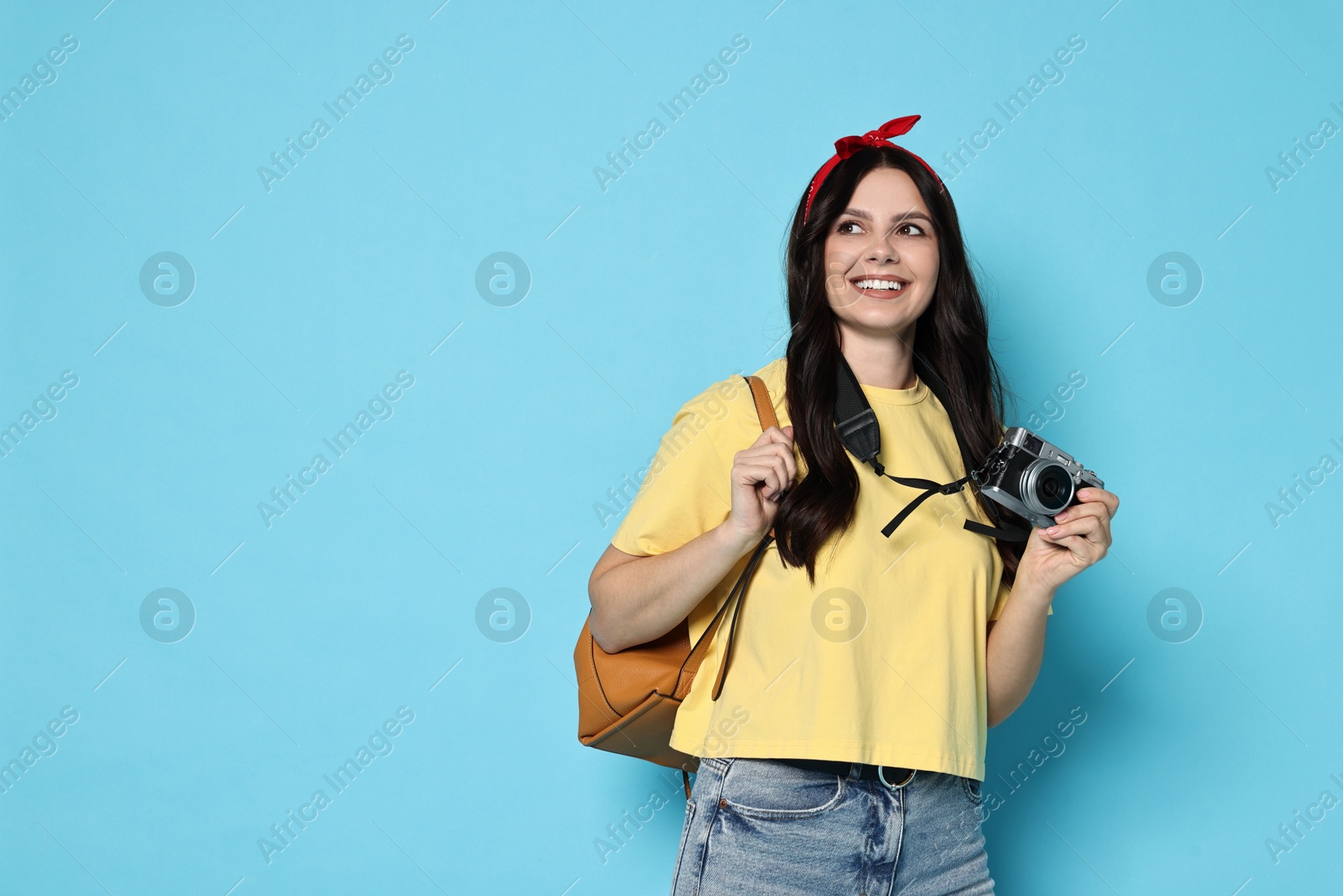 Photo of Young tourist with camera and backpack on light blue background, space for text