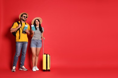 Tourism. Happy couple in hats with suitcase, passports and tickets on red background, space for text