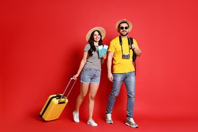 Photo of Tourism. Happy couple in hats with suitcase, passports and tickets on red background