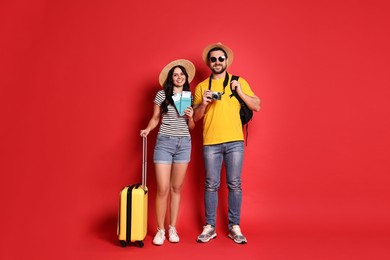 Photo of Tourism. Happy couple in hats with suitcase, passports and tickets on red background