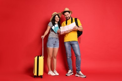 Photo of Tourism. Happy couple in hats with suitcase, passports and tickets on red background