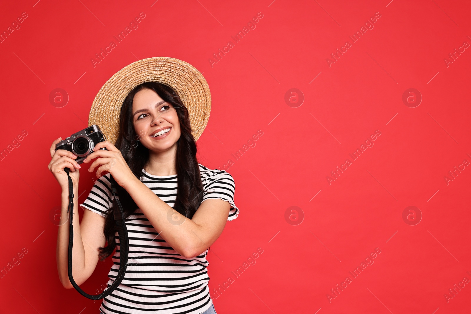 Photo of Young tourist in hat with camera on red background, space for text