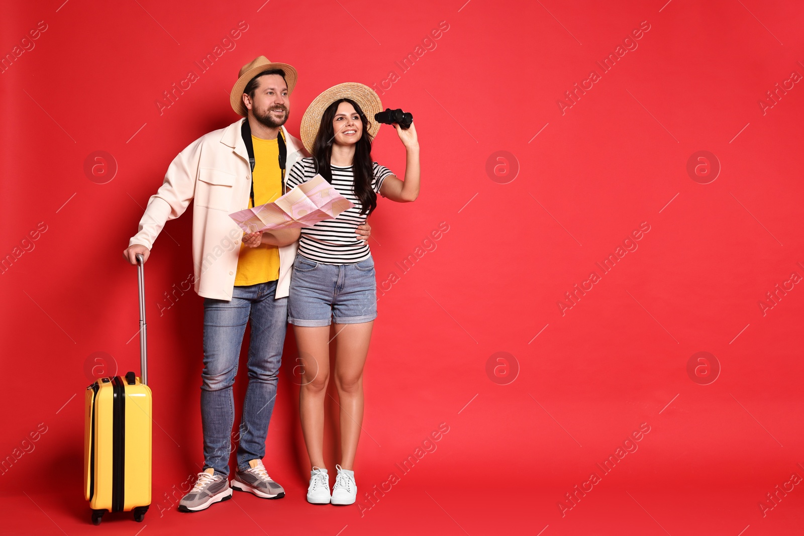 Photo of Tourism. Happy couple in hats with suitcase, map and binoculars on red background