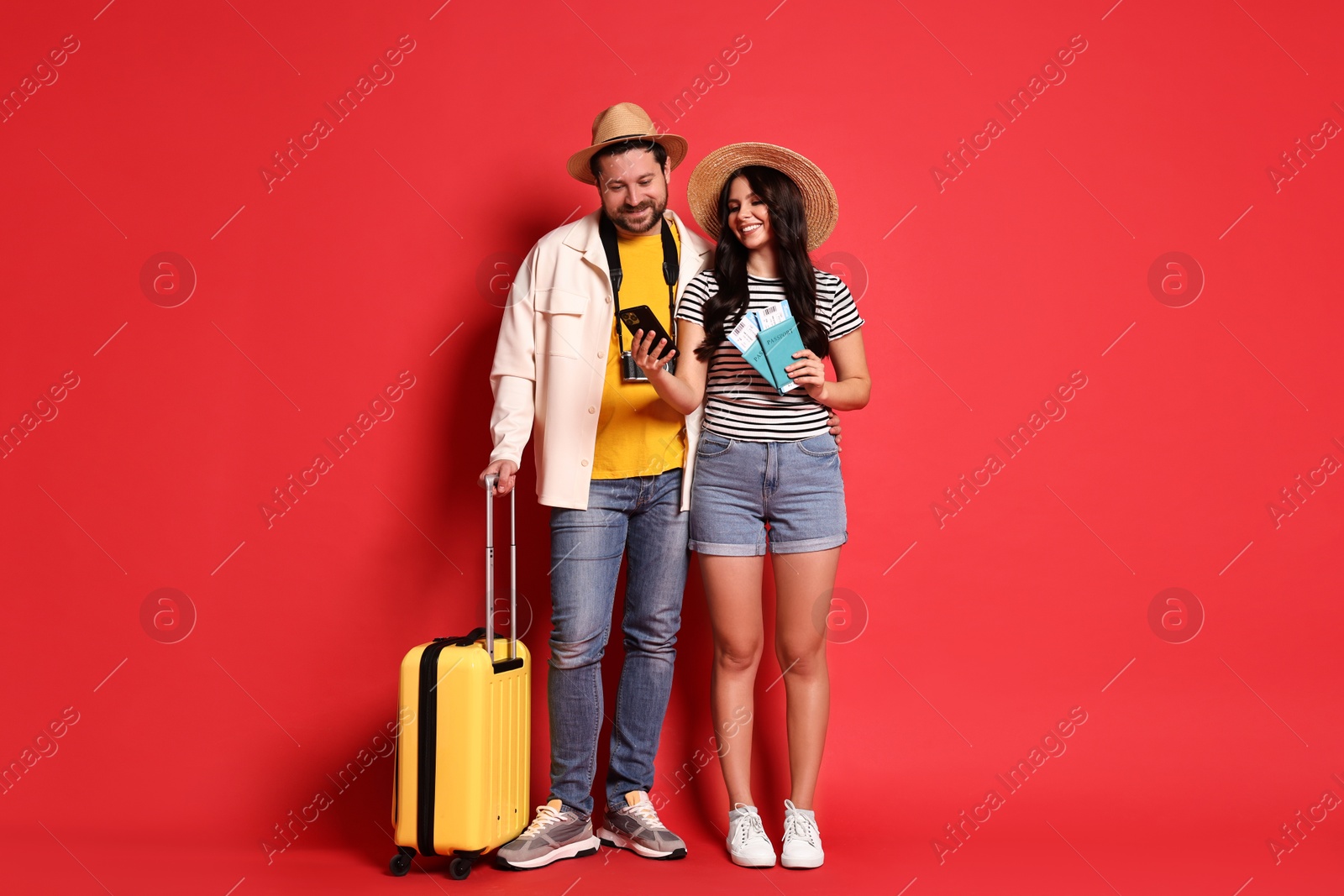 Photo of Tourism. Happy couple in hats with suitcase, passports and tickets on red background