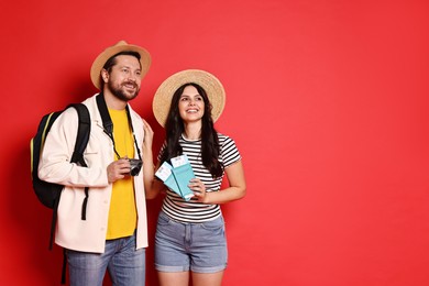 Tourism. Happy couple in hats with camera, passports and tickets on red background, space for text