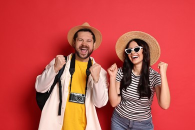 Photo of Tourism. Emotional couple in hats with camera on red background