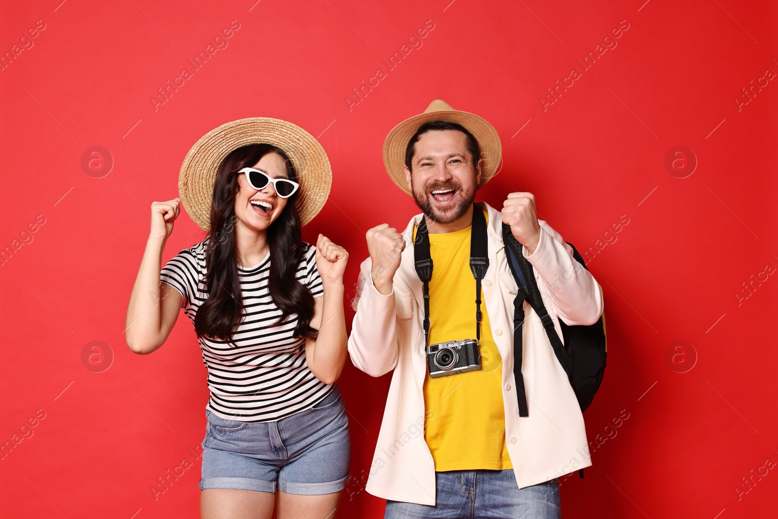 Photo of Tourism. Emotional couple in hats with camera on red background