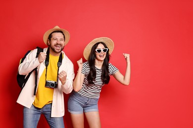 Photo of Tourism. Emotional couple in hats with camera on red background, space for text