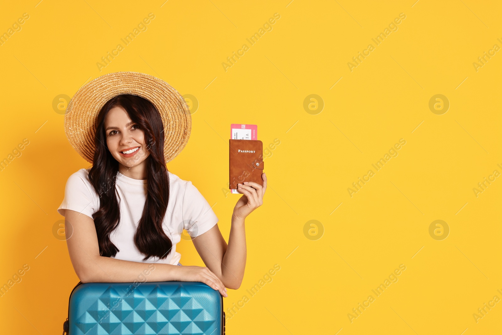 Photo of Young tourist in hat with suitcase, passport and ticket on yellow background, space for text