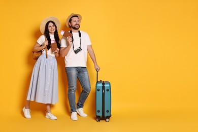 Photo of Tourism. Happy couple in hats with suitcase, passports and tickets on yellow background, space for text