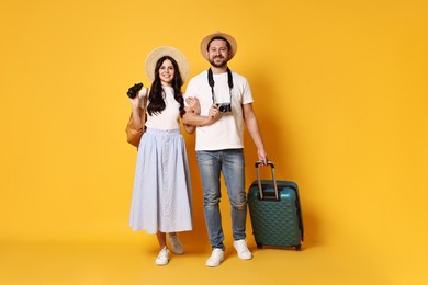 Tourism. Happy couple in hats with suitcase and binoculars on yellow background