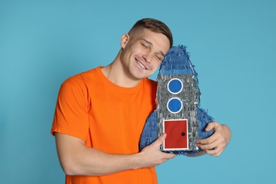 Photo of Happy man with pinata in shape of spaceship on light blue background