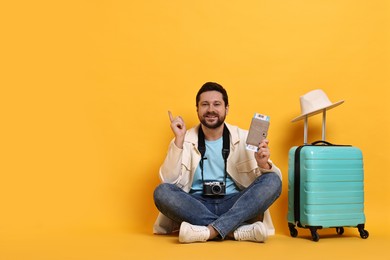 Photo of Traveller with vintage camera, passport, ticket and suitcase on orange background, space for text